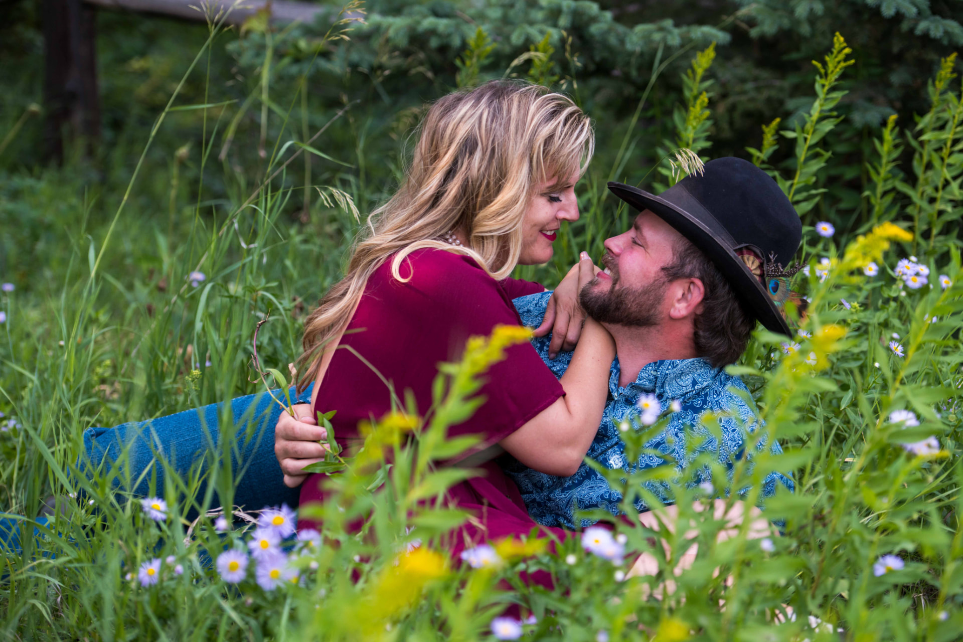 Couple lying in tall grass and wildflowers, smiling closely at one another
