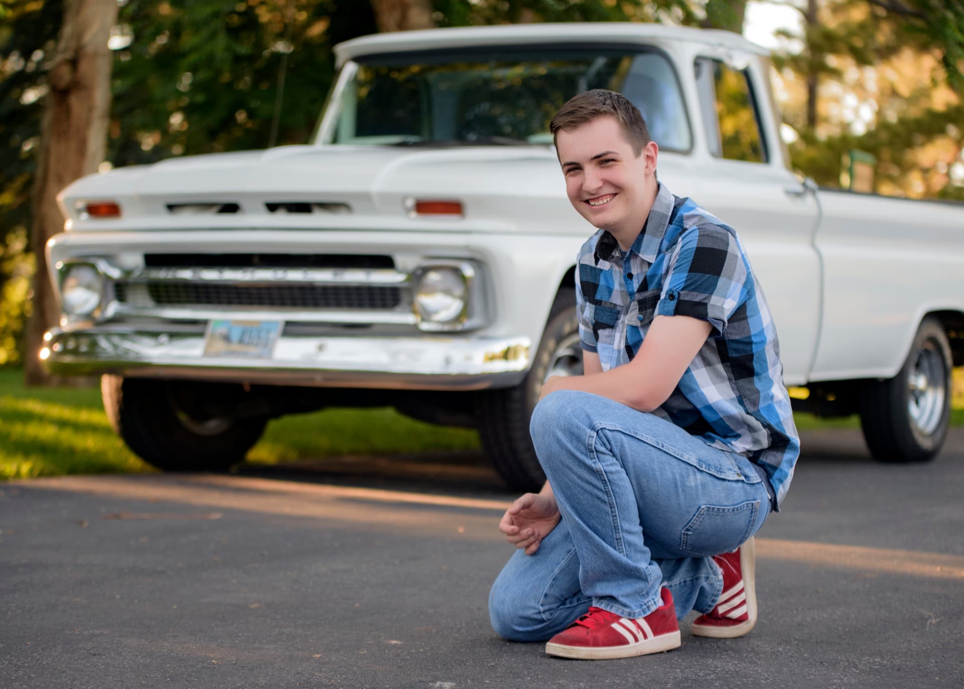 High school senior kneeling and smiling in front of a classic white Chevrolet pickup truck at golden hour