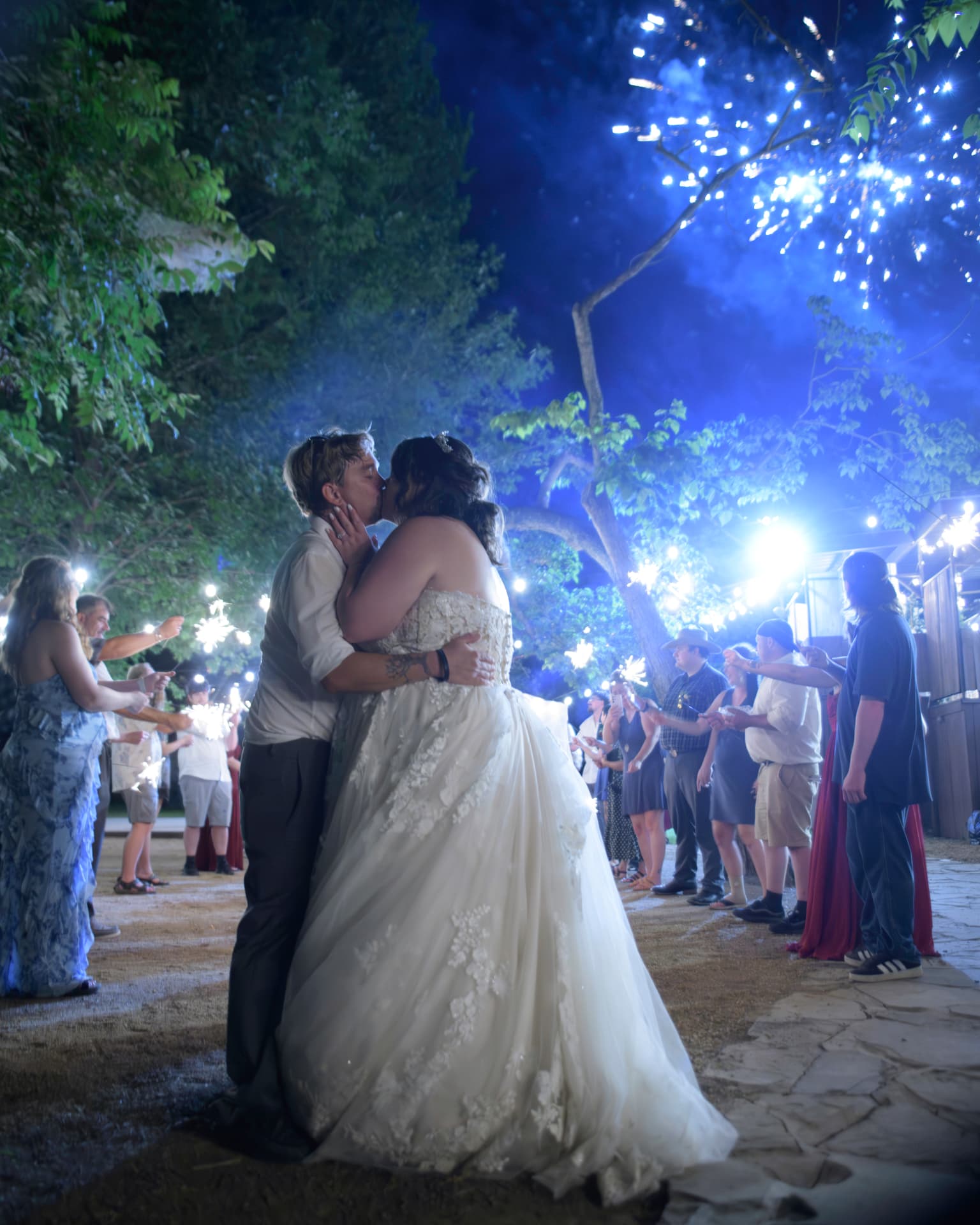 Bride and groom kissing during a nighttime sparkler exit surrounded by guests holding sparklers